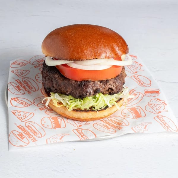 A juicy Alchemist Shack burger with a thick patty, lettuce, tomato, and onion on a brioche bun.