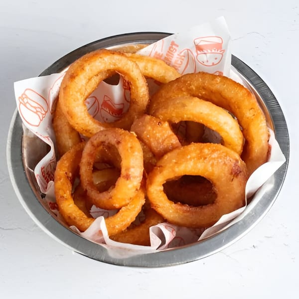 A metal bowl filled with golden-brown, crispy onion rings from The Alchemist Shack.